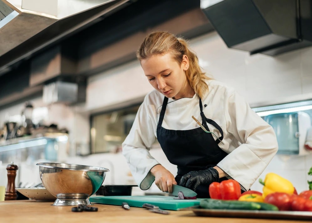 chef mujer en la cocina cortando alimentos, imagen para describir qué significan las siglas APPCC alimentos