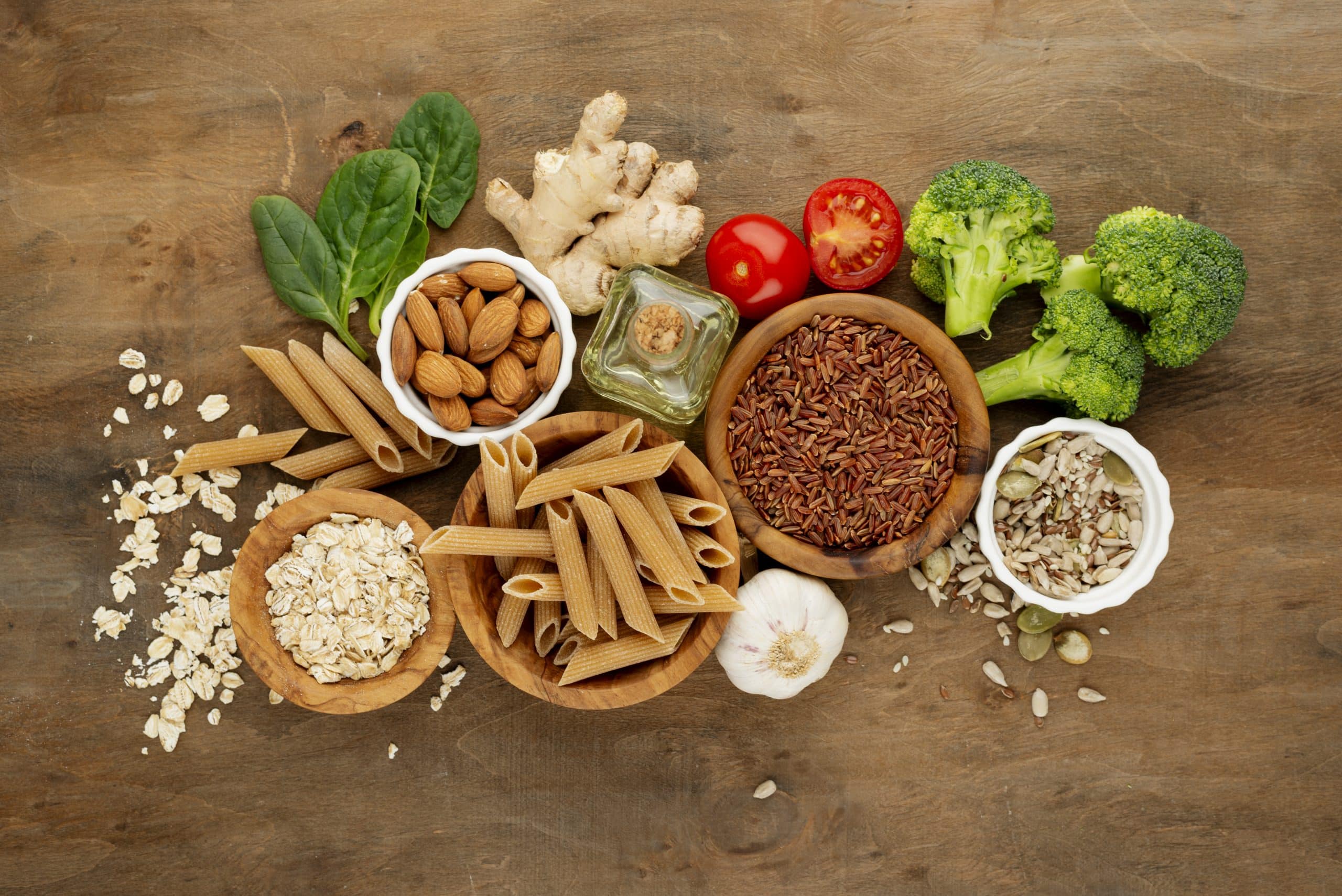 Vista aérea de una serie de alimentos encima de una mesa. Se ve pasta integral, legumbres, brócoli, arroz, tomates, almendras y albahaca. Imagen para el artículo sobre alérgenos en alimentación.